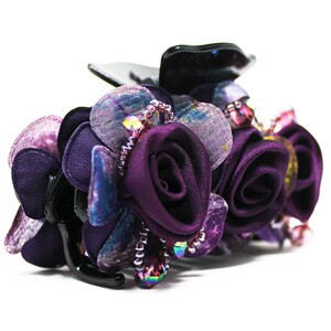 Może przedstawiać: Spinka do włos&oacute;w w kształcie fioletowego kwiatu z czarną podstawą i tęczowymi koralikami.