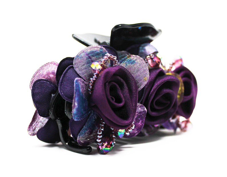 Może przedstawiać: Spinka do włos&oacute;w w kształcie fioletowego kwiatu z czarną podstawą i tęczowymi koralikami.