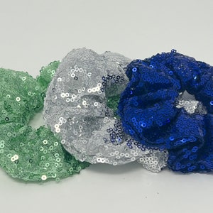May include: Three scrunchies made of sequined fabric. The scrunchies are green, silver, and blue.