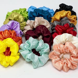 Puede incluir: Una colección de coleteros de satén coloridos en varios tonos, incluyendo amarillo, naranja, morado, verde, azul, turquesa, rosa, beige, burdeos, gris, rojo y negro. Estos accesorios para el cabello están fruncidos y rizados, ofreciendo un aspecto suave y elegante.