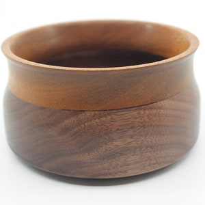 May include: A handcrafted wooden bowl with a two-tone design. The bowl features a dark brown base and a lighter brown rim. The smooth, polished surface highlights the natural wood grain, creating a rustic yet elegant aesthetic. Ideal for serving or display.