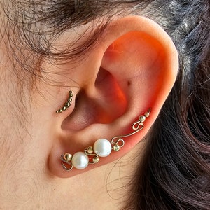 May include: Gold ear cuff with three white pearls and small gold beads. The ear cuff is curved and wraps around the ear.