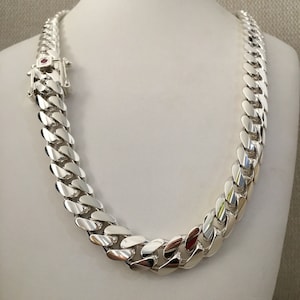 Puede incluir: Un collar de cadena curb plateado con cierre de langosta. La cadena es gruesa y tiene un acabado pulido.