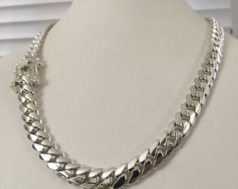 Puede incluir: Un collar de cadena de plata exhibido en un maniquí blanco. El collar presenta una serie de eslabones redondeados entrelazados. El cierre es visible en el lado izquierdo del collar. La cadena es muy reflectante, lo que sugiere un acabado pulido.