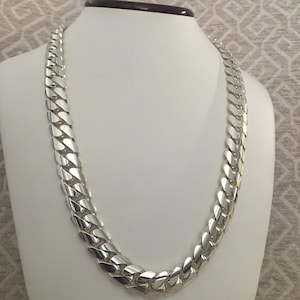 May include: A silver curb chain necklace with a thick, flat link design. The chain is displayed on a white mannequin.