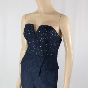 May include: A black strapless jumpsuit with a sequined bodice and a cropped leg. The jumpsuit has a fitted silhouette and a V-neckline.