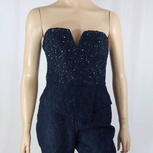 May include: A strapless jumpsuit with a black lace pattern and a beaded bodice. The jumpsuit has a V-neckline and a cropped leg.