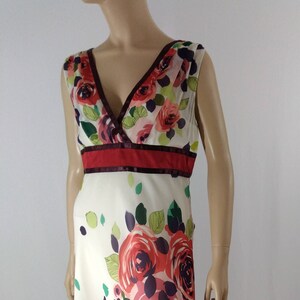 Puede incluir: Un vestido blanco sin mangas con estampado floral con rosas rojas, rosas y moradas. El vestido tiene un escote en V y una cintura roja y burdeos.