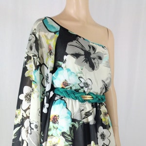 May include: A black and white floral print dress with a one-shoulder design and a teal belt. The dress is made of a sheer fabric and has a flowing silhouette.