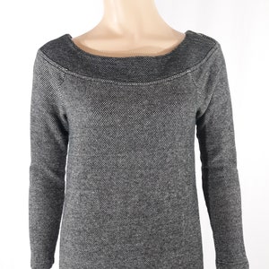 May include: A black and white long-sleeved sweater with a boat neck and a textured pattern. The sweater has a slightly longer hem in the back.