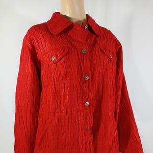 May include: A red quilted jacket with a button-up front and two flap pockets. The jacket has a textured, crinkled fabric.