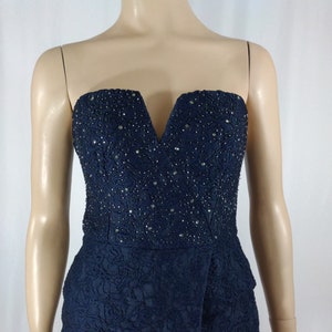 May include: A strapless navy blue jumpsuit with a V-neckline and a beaded bodice. The jumpsuit has a floral pattern and a fitted silhouette.