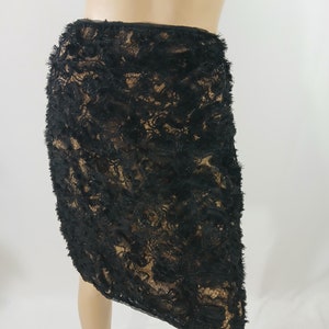 May include: Black lace skirt with a textured, layered design. The skirt is knee-length and features a detailed floral pattern. The skirt is displayed on a mannequin.