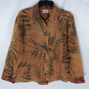 May include: A rust-colored denim jacket with a button-up front and a collared neckline. The jacket features a dark green leaf pattern. The label reads "Chico's Design".