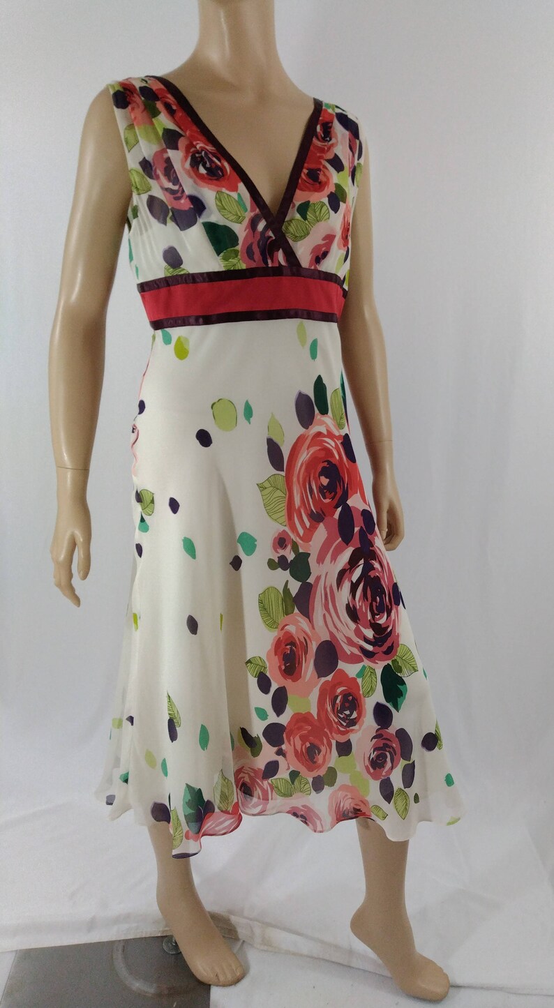 Puede incluir: Un vestido blanco sin mangas con estampado floral con rosas rojas, rosas y moradas. El vestido tiene un escote en V y una cintura roja y burdeos.