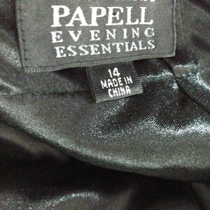 K&ouml;nnte beinhalten: Schwarzes Etikett mit wei&szlig;em Text, der "Adrianna Papell Evening Essentials" lautet, und ein kleineres wei&szlig;es Etikett mit schwarzem Text, der "14 Made in China" lautet.