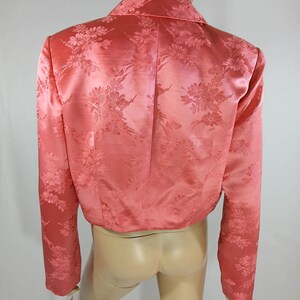 Pu&ograve; includere: Un blazer corto color corallo con motivo floreale. La giacca presenta maniche lunghe, un colletto e una lucentezza satinata. Il motivo floreale &egrave; sottilmente impresso nel tessuto, aggiungendo consistenza e interesse visivo al capo.