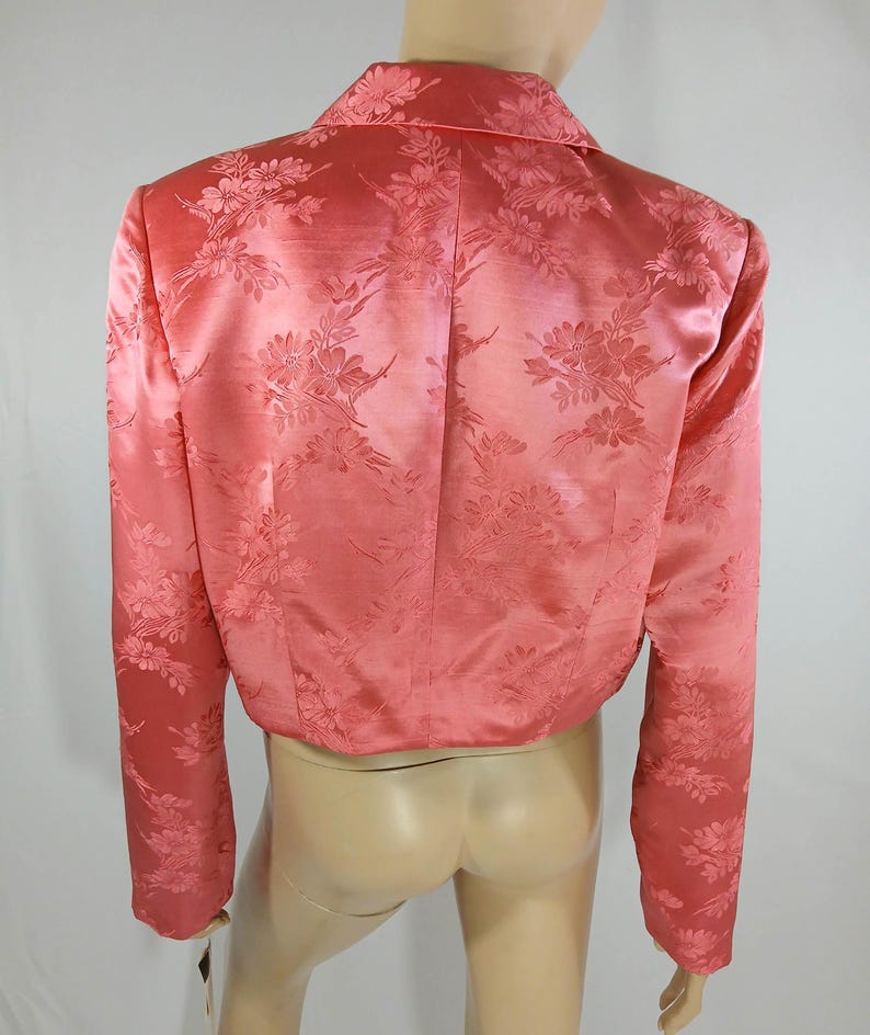 Pu&ograve; includere: Un blazer corto color corallo con motivo floreale. La giacca presenta maniche lunghe, un colletto e una lucentezza satinata. Il motivo floreale &egrave; sottilmente impresso nel tessuto, aggiungendo consistenza e interesse visivo al capo.