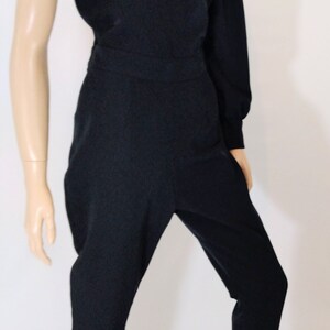 May include: A black one-shoulder jumpsuit with a long sleeve on the right side. The jumpsuit has a fitted bodice and wide-leg pants.