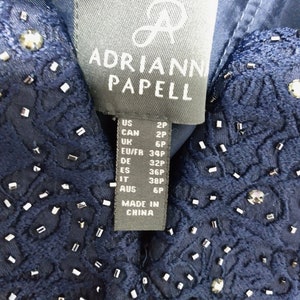 May include: A navy blue dress tag with the brand name "Adrianna Papell" and size information in US, Canadian, UK, EU/FR, German, Spanish, Italian, and Australian sizes. The tag also states "Made in China."