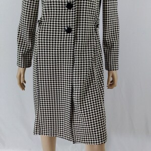May include: A black and white houndstooth patterned coat with a long sleeve and button closure.
