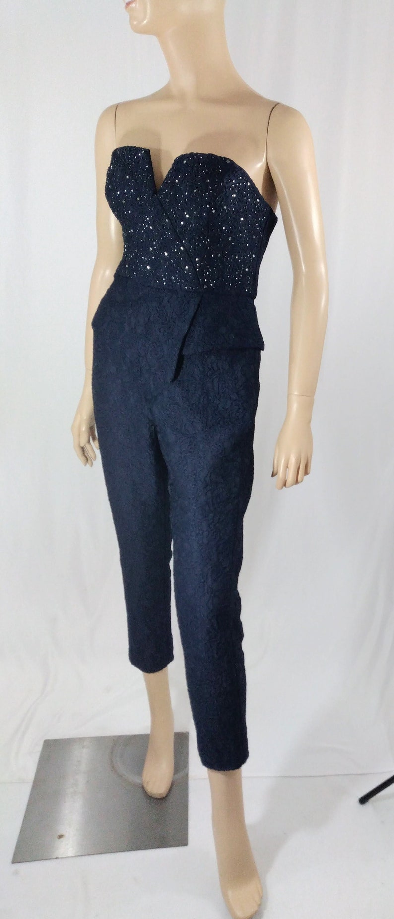 May include: A black strapless jumpsuit with a sequined bodice and a cropped leg. The jumpsuit has a fitted silhouette and a V-neckline.
