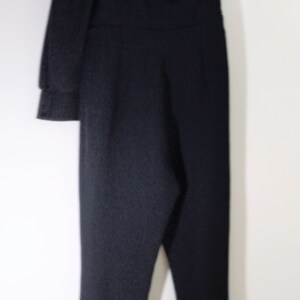 May include: A black one-shoulder jumpsuit with a long sleeve on one side and a short sleeve on the other side.