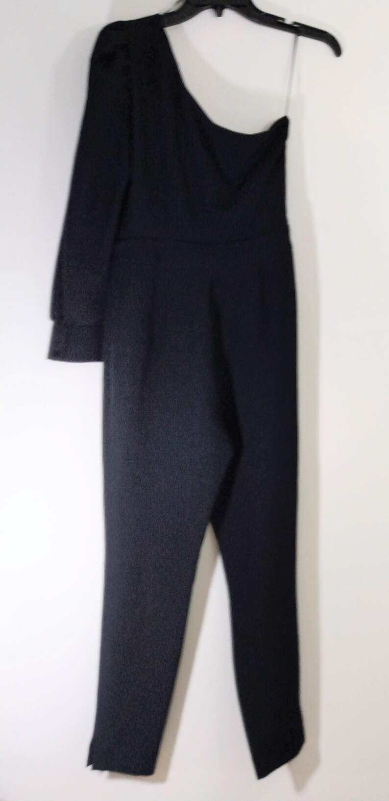 May include: A black one-shoulder jumpsuit with a long sleeve on one side and a short sleeve on the other side.