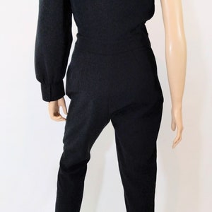 May include: A black one-shoulder jumpsuit with a long sleeve on the left side. The jumpsuit has a fitted bodice and wide-leg pants.