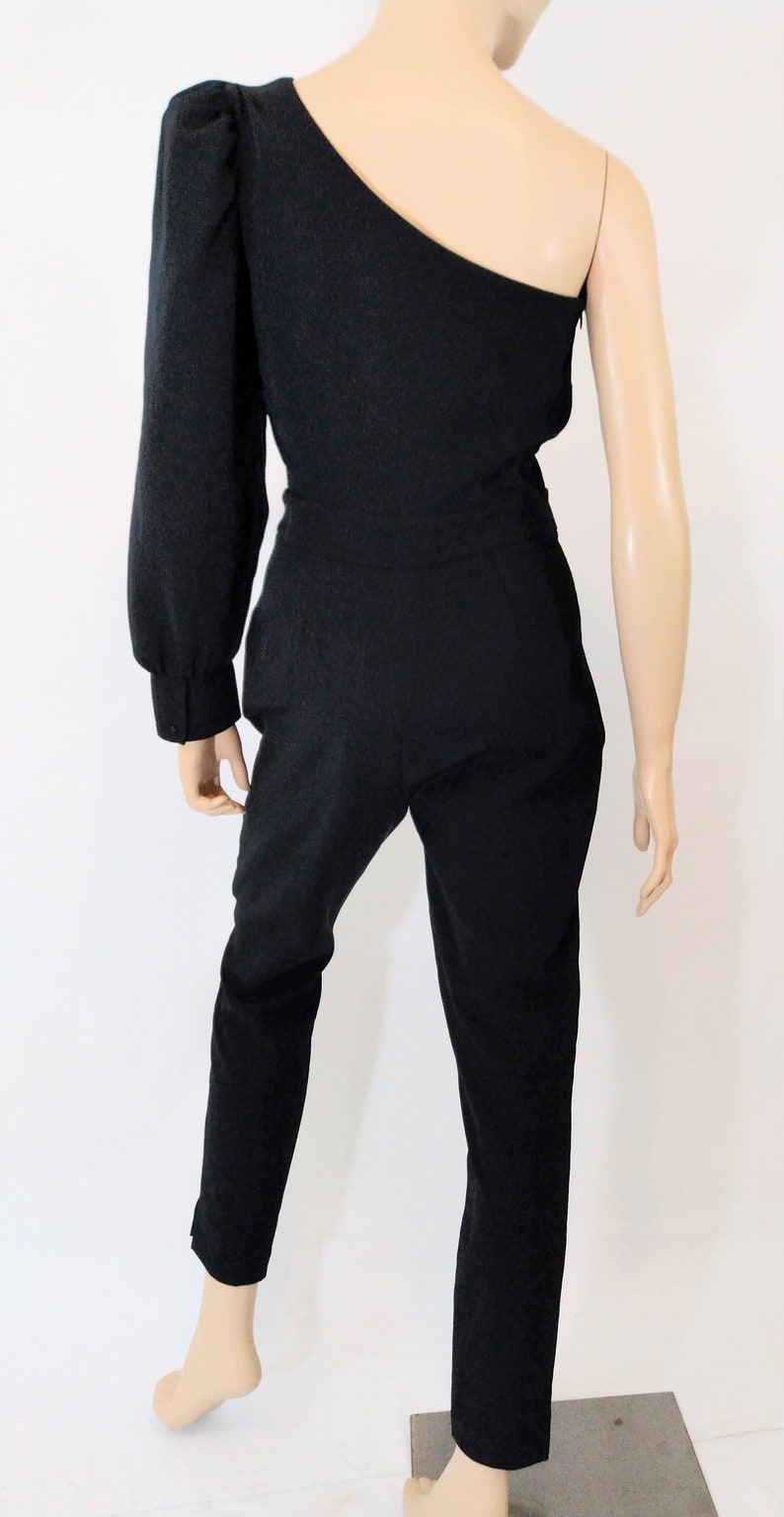 May include: A black one-shoulder jumpsuit with a long sleeve on the left side. The jumpsuit has a fitted bodice and wide-leg pants.