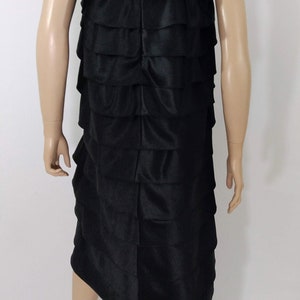 K&ouml;nnte beinhalten: Ein schwarzes tr&auml;gerloses Kleid mit einem mehrstufigen R&uuml;schen-Design. Das Kleid ist aus einem glatten, seidenartigen Stoff gefertigt.