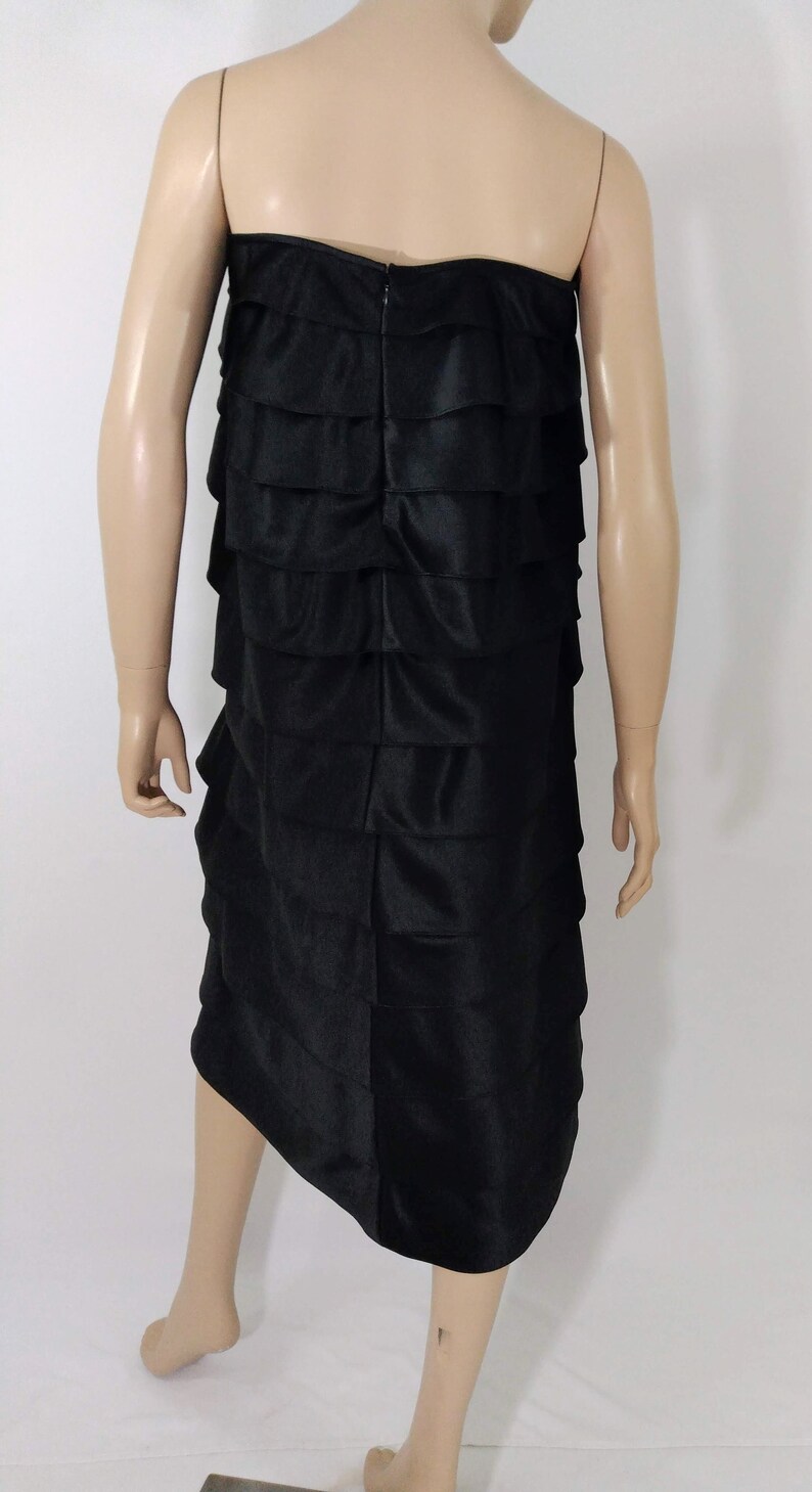 K&ouml;nnte beinhalten: Ein schwarzes tr&auml;gerloses Kleid mit einem mehrstufigen R&uuml;schen-Design. Das Kleid ist aus einem glatten, seidenartigen Stoff gefertigt.