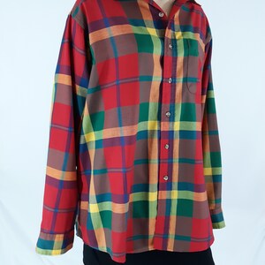 May include: A long-sleeved plaid shirt with a button-up front. The shirt is red, green, yellow, and brown.