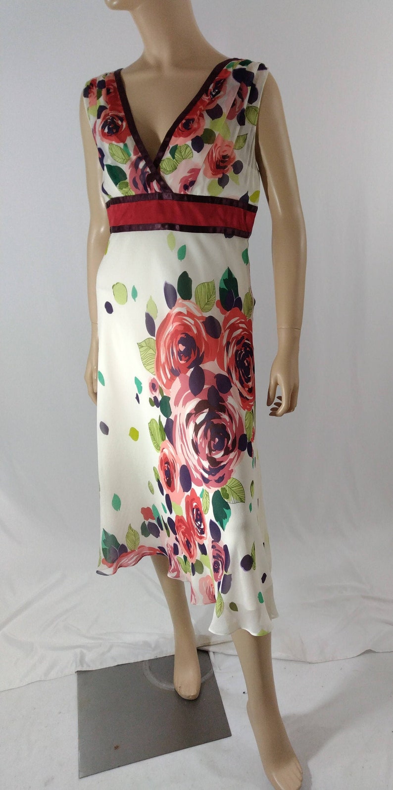 Puede incluir: Un vestido blanco sin mangas con estampado floral con rosas rojas, rosas y moradas. El vestido tiene un escote en V y una cintura roja y burdeos.