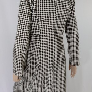 May include: A black and white houndstooth patterned coat with a long sleeve and a collar.