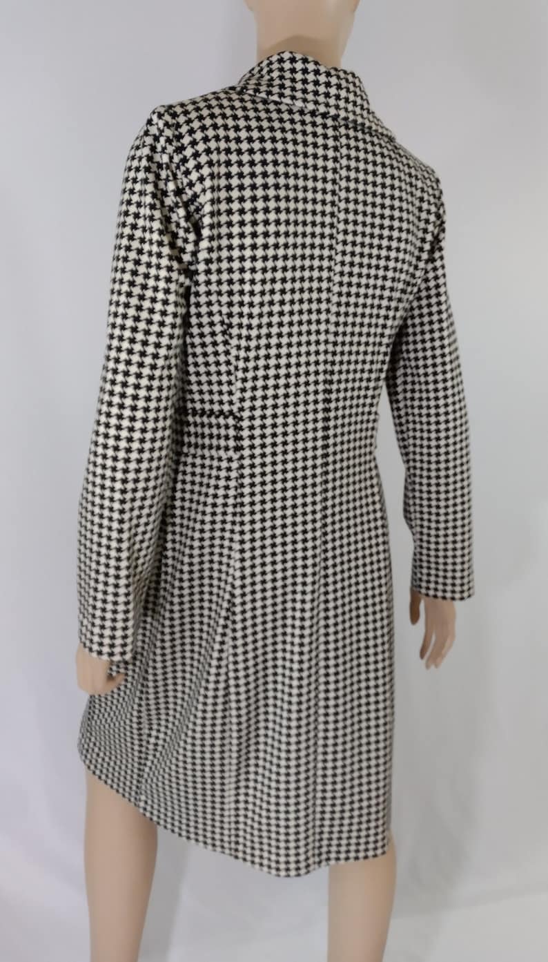 May include: A black and white houndstooth patterned coat with a long sleeve and a collar.