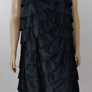 K&ouml;nnte beinhalten: Ein schwarzes, tr&auml;gerloses Kleid mit einem mehrstufigen R&uuml;schenrock. Der Rock ist aus einem glatten, seidenartigen Stoff.