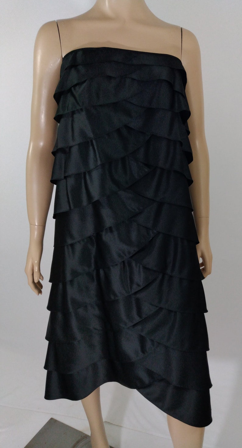K&ouml;nnte beinhalten: Ein schwarzes, tr&auml;gerloses Kleid mit einem mehrstufigen R&uuml;schenrock. Der Rock ist aus einem glatten, seidenartigen Stoff.