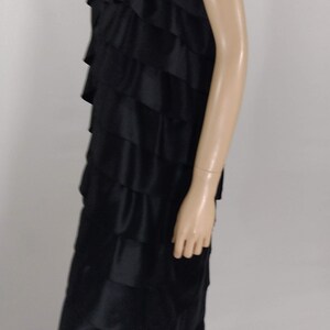 K&ouml;nnte beinhalten: Ein schwarzes tr&auml;gerloses Kleid mit mehreren R&uuml;schenlagen. Das Kleid ist aus seidenartigem Stoff und hat ein tailliertes Oberteil.