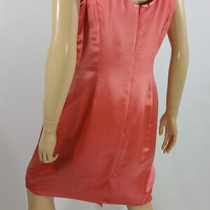Pu&ograve; includere: Abito senza maniche color corallo con scollatura rotonda. L'abito &egrave; realizzato in un materiale lucido, simile al raso, e ha una silhouette semplice e aderente. L'abito &egrave; lungo fino al ginocchio e ha un piccolo spacco sul retro.