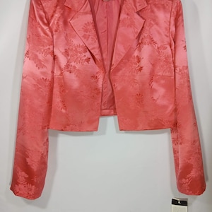 Pu&ograve; includere: Un blazer color corallo con motivo floreale. La giacca ha maniche lunghe e colletto a revers. L'etichetta recita "Adrianna Papell". Un'etichetta taglia 12 &egrave; appesa alla giacca.