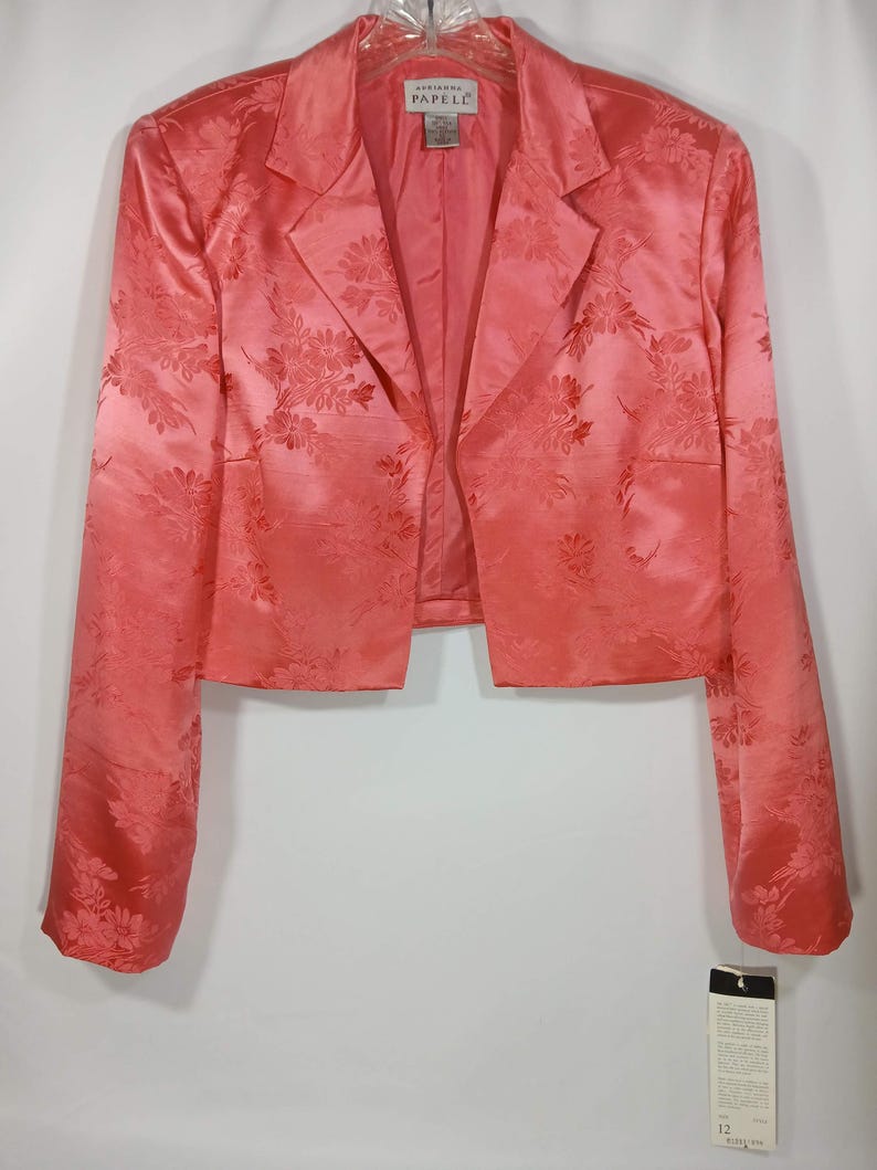 Pu&ograve; includere: Un blazer color corallo con motivo floreale. La giacca ha maniche lunghe e colletto a revers. L'etichetta recita "Adrianna Papell". Un'etichetta taglia 12 &egrave; appesa alla giacca.