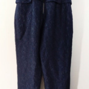 May include: A dark blue, sleeveless jumpsuit with a zipper closure in the back. The jumpsuit has a textured fabric and a fitted silhouette.