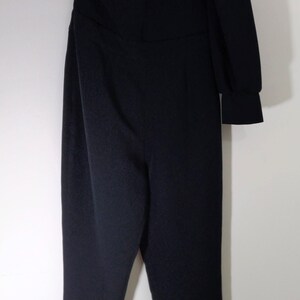 May include: A black one-shoulder jumpsuit with long sleeves. The jumpsuit has a fitted bodice and wide-leg pants.