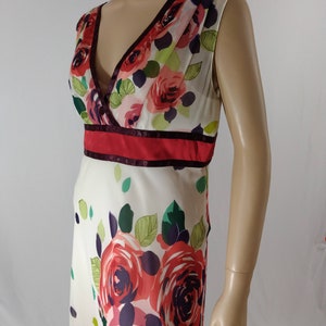 Puede incluir: Un vestido blanco sin mangas con estampado floral de rosas rojas, rosas y moradas. El vestido tiene un escote en V y una cintura roja y burdeos.