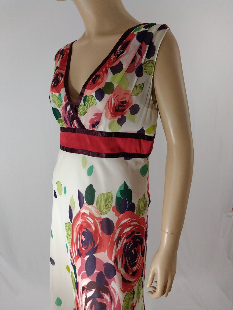 Puede incluir: Un vestido blanco sin mangas con estampado floral de rosas rojas, rosas y moradas. El vestido tiene un escote en V y una cintura roja y burdeos.