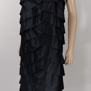 K&ouml;nnte beinhalten: Ein schwarzes tr&auml;gerloses Kleid mit mehreren R&uuml;schenlagen. Das Kleid ist knielang und hat einen leicht asymmetrischen Saum.