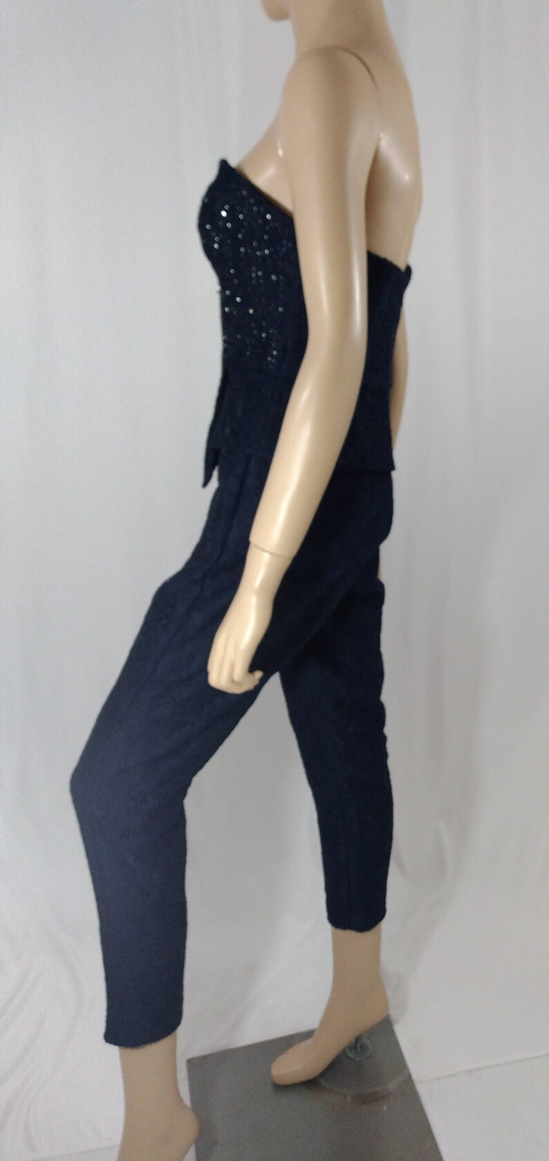 May include: A strapless black jumpsuit with a sequined bodice. The jumpsuit is made of a textured fabric and has a fitted silhouette.