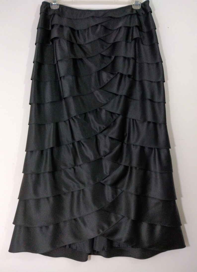 K&ouml;nnte beinhalten: Ein schwarzer Satinrock mit mehreren R&uuml;schenlagen. Der Rock ist bodenlang und hat ein schlichtes, elegantes Design.