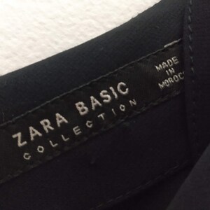 May include: A black Zara Basic Collection tag with white text that reads "Zara Basic Collection" and "Made in Morocco".